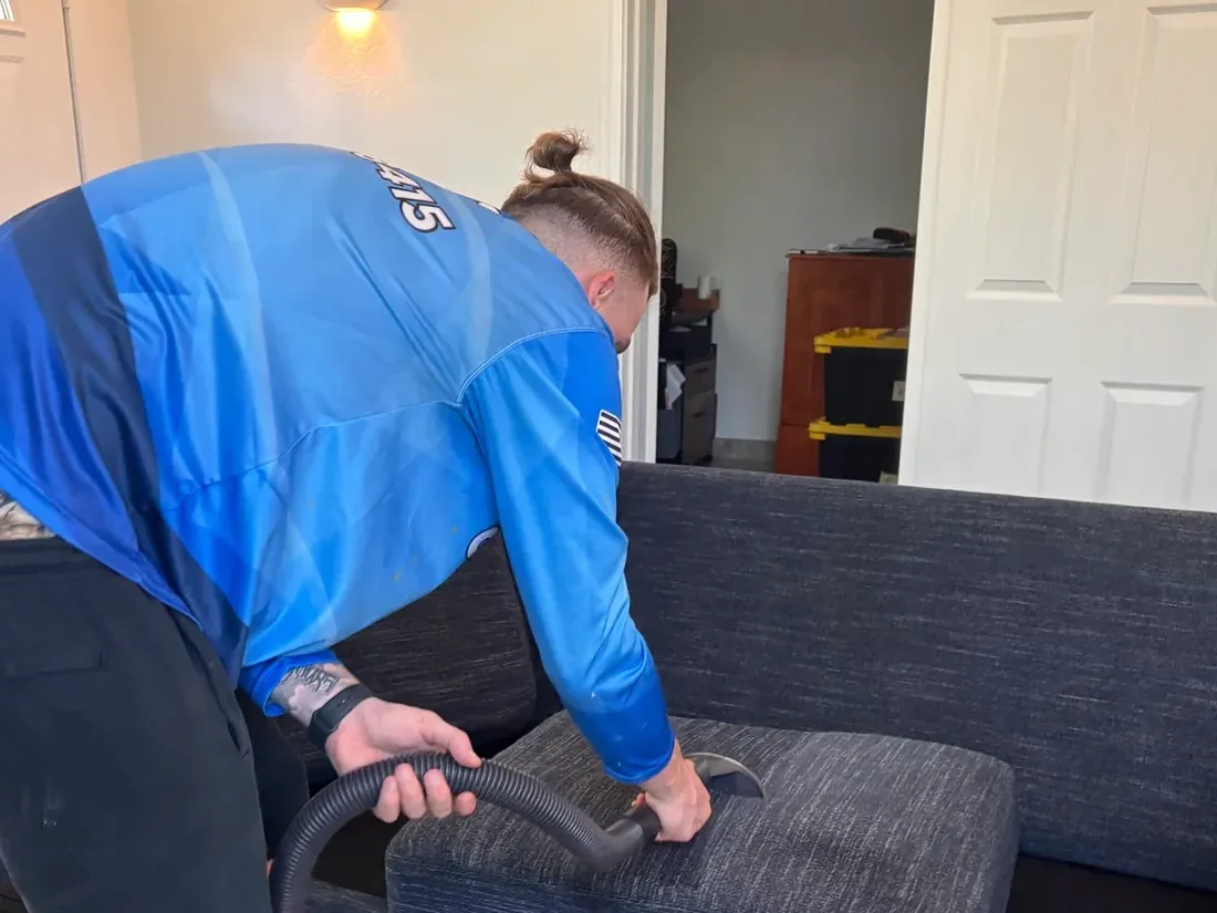 Technician extracting a gray fabric sofa cushion with an upholstery tool